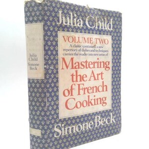 May include: A hardcover cookbook titled "Mastering the Art of French Cooking, Volume Two" by Julia Child and Simone Beck. The book has a blue cover with a floral pattern and a central panel with the title in red and white.