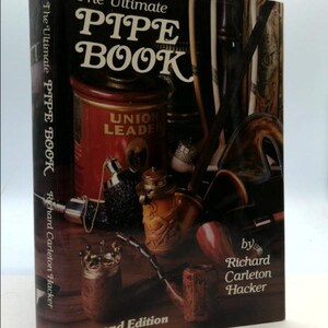 May include: The Ultimate Pipe Book, second edition, by Richard Carleton Hacker. The book cover features a variety of pipes and tobacco paraphernalia, including a tin of Union Leader tobacco.