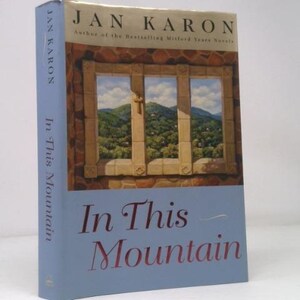 May include: A hardcover book titled "In This Mountain" by Jan Karon. The cover features a window overlooking a mountain landscape. The spine is light blue with the author's name and book title. The book is a novel.