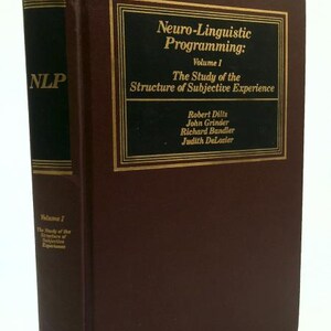 May include: A hardcover book titled "Neuro-Linguistic Programming: Volume 1" with the subtitle "The Study of the Structure of Subjective Experience." The book is brown with gold lettering and accents. The spine reads "NLP."