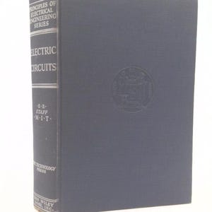 May include: A hardcover book titled "Electric Circuits" from the "Principles of Electrical Engineering Series." The book has a dark blue cover with a subtle embossed design and a spine with white text. Published by John Wiley & Sons, Inc.