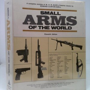 May include: A book titled "Small Arms of the World" by Edward Clinton Ezell. The cover features illustrations of various firearms, including a pistol and rifles. The eleventh edition of the book is visible.