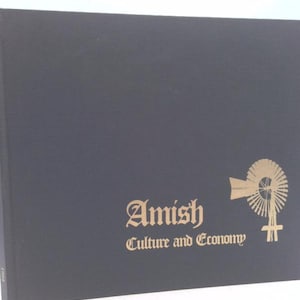 May include: A dark blue book titled "Amish Culture and Economy" with gold lettering and a windmill illustration. The book's cover has a textured appearance, and the title is in a decorative font.