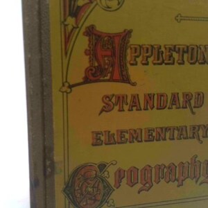 May include: A vintage book with a yellow cover featuring the title "Appleton's Standard Elementary Geography" in ornate lettering. The cover has decorative elements in red and gold, with a textured spine.