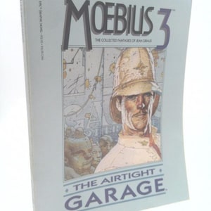 May include: A paperback book titled "Moebius 3: The Airtight Garage" featuring a detailed illustration of a man in a safari hat. The cover is light blue with the title in large, stylized letters and the author's name.