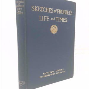 May include: A navy blue book titled "Sketches of Froebel's Life and Times" with gold lettering. The book is from the National Library of Kindergarten Literature and published by Milton Bradley Co.