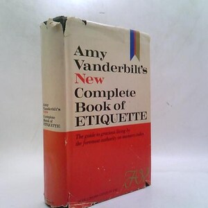 May include: A hardcover book titled "Amy Vanderbilt's New Complete Book of Etiquette." The book has a cream-colored cover with red and black text. A red band is at the bottom. The book's spine has a blue, red, and gold ribbon.