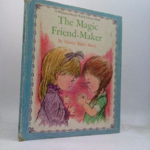 May include: A vintage children's book titled "The Magic Friend-Maker" by Gladys Baker Bond. The cover features illustrations of two young girls in a soft, pastel color palette. The book has a light blue border with the text "A Whitman Small World Library Book".