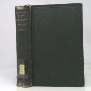 May include: An antique book with a dark green cover and the title "Behrens' Guide to the Microscope in Botany" visible on the spine. The book's cover shows signs of wear, with a faded appearance and some damage to the edges.