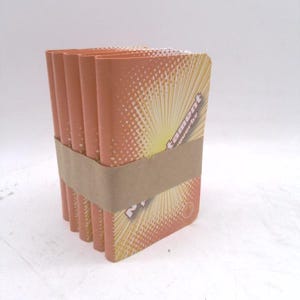 May include: A stack of orange and yellow rectangular items, bound together with a brown band. The items have a sunburst design and the word "tament" is visible.