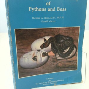 May include: A blue hardcover book titled The Reproductive Husbandry of Pythons and Boas by Richard A. Ross, M.D., M.P.H. and Gerald Marzec. The cover features a photograph of a dark snake emerging from white eggs on a wooden surface.