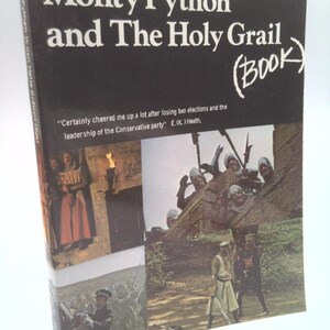 May include: A black book titled Monty Python and The Holy Grail (Book) with white text. The cover features a quote by E. (K.) Heath and three photographic scenes from the film showing characters in medieval costumes and military uniforms.