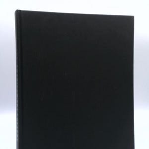 May include: A black book with a matte finish. The book is rectangular and appears to be closed, with the spine visible on the left side. The cover is a solid, dark color, and the edges are clean and sharp.
