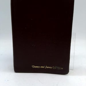 May include: A dark brown leather-bound book with rounded corners. The text "Danny and Jamie" is printed in gold on the lower right corner. The book appears to be closed and in good condition.