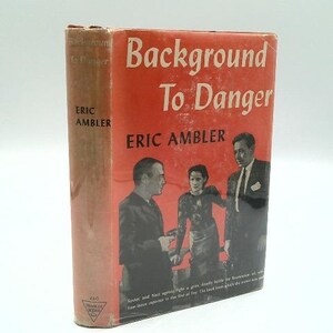 May include: A vintage hardcover book titled "Background To Danger" by Eric Ambler. The cover is predominantly red with white lettering and features illustrations of three people. The spine is a faded brown color.