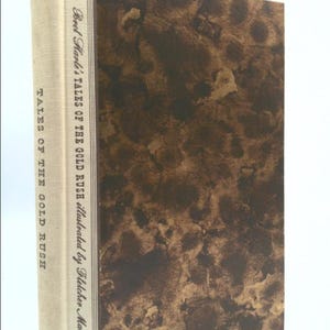 May include: A brown book with a white spine. The spine has the title "Brel Harle's Tales of the Gold Rush" and the text "illustrated by Fletcher Marlin".