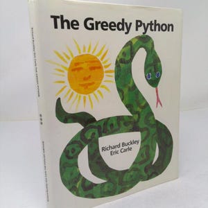 May include: A hardcover children's book titled The Greedy Python by Richard Buckley and Eric Carle. The white cover features a large green snake with dark green spots, a yellow sun with a face, and black text displaying the title and authors.