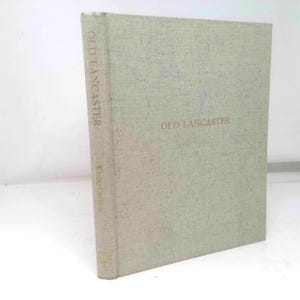 May include: A hardcover book titled "OLD LANCASTER" in a light beige color. The book's spine displays the title vertically. The cover has a textured appearance. The book is standing upright against a white background.
