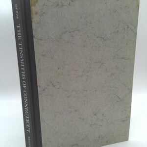May include: A gray book with a black spine. The spine has the text "DAVOR - THE TINSMITHS OF CONNECTICUT - WEALEY" printed on it.