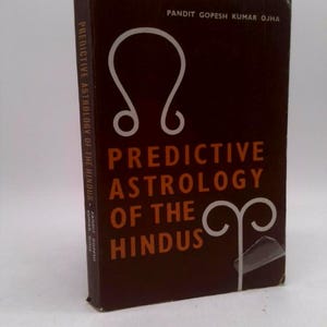May include: A hardcover book titled "Predictive Astrology of the Hindus" by Pandit Gopesh Kumar Ojha. The cover is dark brown with white astrological symbols and orange text. The book's spine also has text.