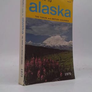 May include: A vintage travel guide titled "Guide to Alaska" by Lou Jacobin. The cover features a yellow background with blue text, and a landscape photo of mountains, flowers, and a lake. The year 1975 is printed on the cover.
