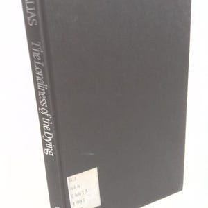May include: A hardcover book titled "The Loneliness of the Dying" by Elias. The book has a dark gray cover with the title and author's name printed vertically on the spine. A white sticker with text is affixed to the back.