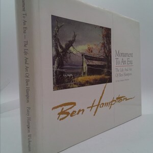 May include: Book cover with a painting of a farmhouse in a field with a tree in the foreground. The title of the book is "Monument To An Era - The Life And Art Of Ben Hampton" by Patsy Hampton Wichmann. The author's name is written in cursive in gold lettering.