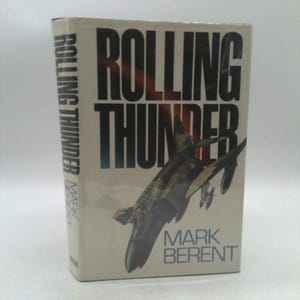 May include: A book titled "Rolling Thunder" by Mark Berent. The cover features a black and white illustration of a fighter jet.