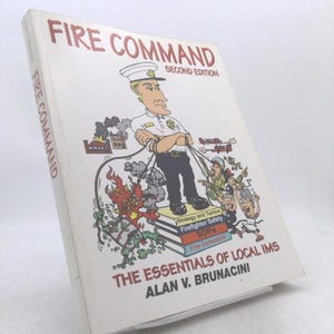 May include: A white softcover book titled Fire Command Second Edition by Alan V. Brunacini. The cover features a cartoon illustration of a firefighter standing on a stack of books labeled Strategy and Tactics, Firefighter Safety, SOPs, and Fire Command.