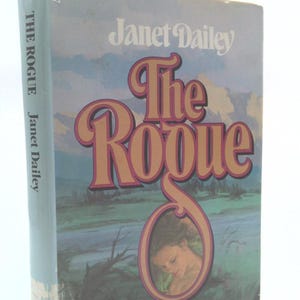 May include: A vintage paperback book titled "The Rogue" by Janet Dailey. The cover features a woman with long brown hair and a blue and green landscape.