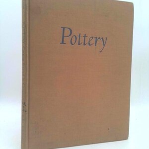 May include: A brown book with the title "Pottery" printed in blue on the front cover.