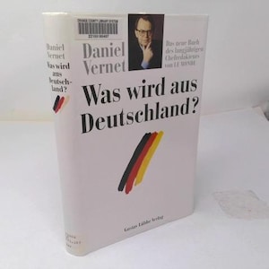 May include: A hardcover book titled Was wird aus Deutschland? by Daniel Vernet with a white dust jacket. The cover features a black, red, and yellow diagonal brushstroke graphic, a small portrait of the author, and a library barcode sticker at the top.
