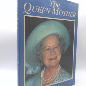 May include: A hardcover book titled "The Queen Mother" by Helene McGowan. The cover is blue with a portrait of a smiling woman wearing a hat and pearls. The book's spine also features the title and author.