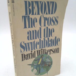 May include: A book cover with a beige background and blue text that reads "Beyond The Cross and the Switchblade" by David Wilkerson. The cover features a black and white illustration of a person holding a switchblade in front of a church.