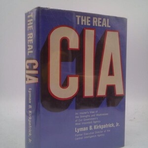 May include: A hardcover book titled "THE REAL CIA" with large red and white lettering on a blue background. The book's spine reads "THE REAL CIA" and the author's name is Lyman B. Kirkpatrick, Jr.