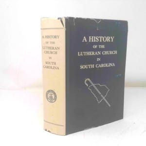 May include: A hardcover book titled "A History of the Lutheran Church in South Carolina." The book has a black cover with white text and a graphic of a cane and the state outline. The spine is cream-colored with text.