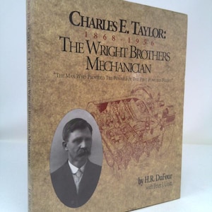 May include: A book titled "Charles E. Taylor: The Wright Brothers Mechanician" with a portrait of Charles E. Taylor. The cover is tan with black and red text and a detailed illustration of an engine. The book is by H.R. DuFour with Peter L. Unitt.