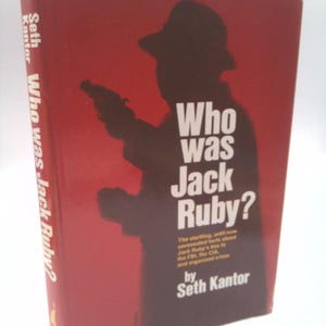 May include: A hardcover book titled "Who Was Jack Ruby?" by Seth Kantor. The cover is red with a dark silhouette of a person holding a gun. The title is in large white letters.