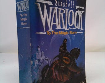 May include: A paperback book cover with a blue background and a fantasy illustration of a man riding a horse. The title of the book is "Warlock: To The Magic Born" by Christopher Stasheff.