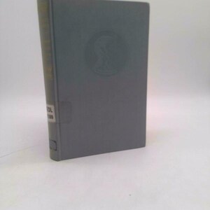 May include: A hardcover book with a gray cover and a circular embossed design. The spine is a lighter color with text. The book is standing upright against a white background.