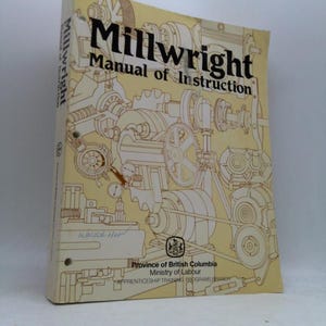 May include: A vintage "Millwright Manual of Instruction" book. The cover is beige with a detailed illustration of machinery in brown. The title is in bold black letters. The book is from the Province of British Columbia, Ministry of Labour.