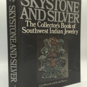 May include: A hardcover book titled "SKYSTONE AND SILVER" with the subtitle "The Collector's Book of Southwest Indian Jewelry." The cover is black with white lettering and a detailed illustration of jewelry. The author's names, Carl Rosnek and Joseph Stacey, are also visible.