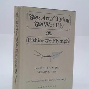May include: A hardcover book titled "The Art of Tying the Wet Fly & Fishing the Flymph." The cover is a light beige color with black text and illustrations of a fly. The book is by James E. Leisenring and Vernon S. Hidy.