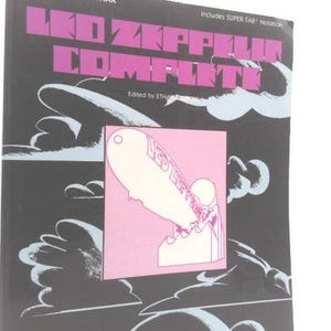 May include: A black book titled "Led Zeppelin Complete" with purple text. The cover features a pink square with a white illustration of a zeppelin and a figure. Includes Super-TAB Notation.