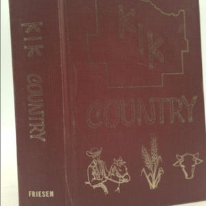 May include: A red book with the title "KIK COUNTRY" in gold lettering. The book cover features a stylized map of a state with the word "KIK" inside. There are illustrations of a cowboy on a horse, wheat stalks, and a cow.