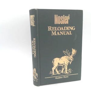 May include: A black "Nosler Reloading Manual" book with gold lettering and a gold illustration of a moose. The spine reads "Reloading Manual" vertically. The book is labeled "Number Three".