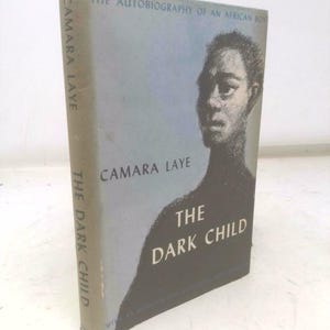 May include: A hardcover book titled "The Dark Child" by Camara Laye. The cover features a portrait of a person and the title in white text against a blue background. The spine also displays the title and author.