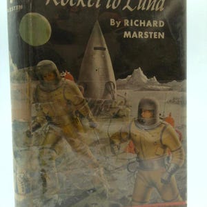 May include: Vintage book cover titled "Rocket to Luna" by Richard Marsten. The cover art depicts two astronauts in yellow space suits, a silver rocket, and a green planet against a dark background. The book is in a vertical format.