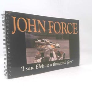 May include: A spiral-bound book with a black cover featuring the name "JOHN FORCE" in orange lettering. The cover includes a photo of a race car and the text "I saw Elvis at a thousand feet".