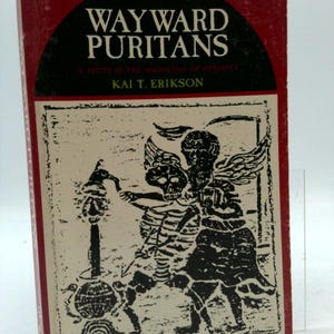 May include: A hardcover book titled "WAYWARD PURITANS" with a red cover and black text. The book's cover features a black and white illustration of skeletal figures. The author's name, Kai T. Erikson, is also visible.